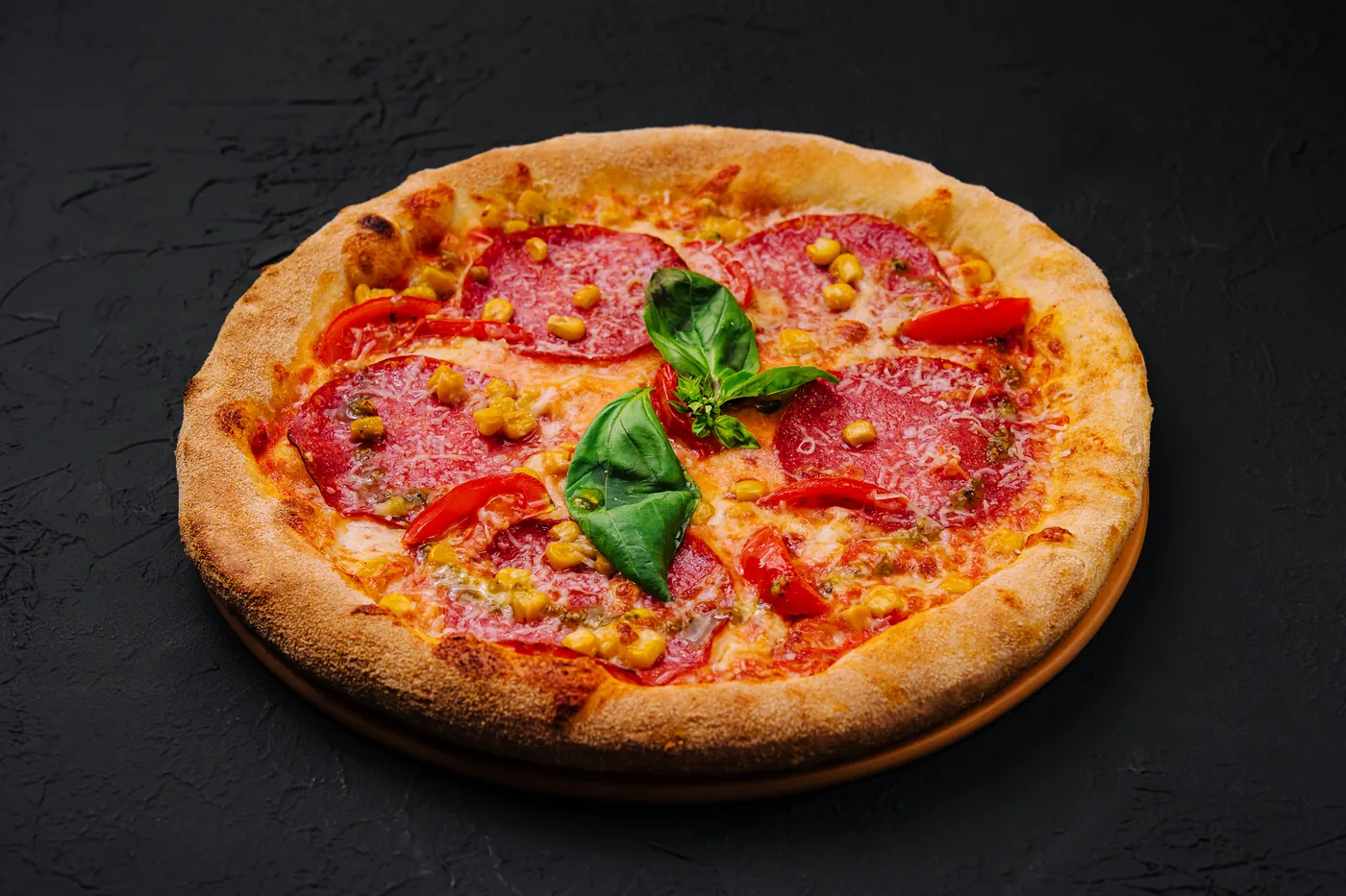 Pizza with salami, tomatoes, basil and corn on a dark background